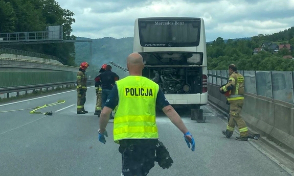 uszkodzony autobus stojący na drodze, obok niego strażacy, w stronę autokaru idzie policjant