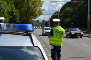 Zdjęcie poglądowe, przedstawiające policjanta, który urządzeniem do pomiaru prędkości sprawdza prędkość jadących samochodów.