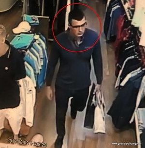 Zdjęcie poglądowe, przedstawiające mężczyznę w okularach, który znajduje się w sklepie z odzieżą. Mężczyzna trzyma w dłoni dwie papierowe torby.