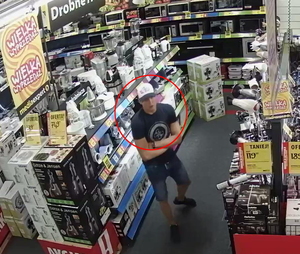 Zdjęcie poglądowe, przedstawiające sprawce kradzieży sprzętu elektronicznego. Mężczyzna stoi w sklepie elektronicznym z założonymi rękoma i obserwuje towar na półkach.