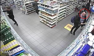 Zdjęcie poglądowe, przedstawiające mężczyznę podejrzewanego o kradzież perfum. Mężczyzna jest w sklepie. Stoi przed regałami i patrzy na kamerę.