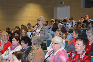 Zdjęcie poglądowe, przedstawiające publiczność, podczas debaty z seniorami. Na zdjęciu wśród seniorek stoi jedna z nich i mówi do mikrofonu.