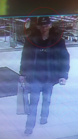 Zdjęcie poglądowe, przedstawiające mężczyznę w centrum handlowym. Mężczyzna ma na sobie ciemne ubrania i ciemną czapkę z daszkiem, a w ręku trzyma torbę.