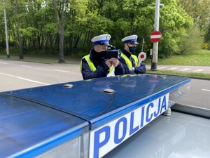 Zdjęcie przedstawiające dwóch policjantów ruchu drogowego podczas pomiaru prędkości nadjeżdżającym samochodom.