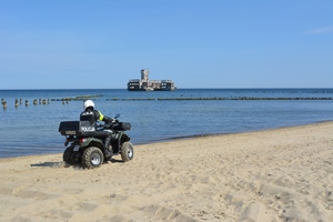 Zdjęcie przedstawiające policjanta na quadzie. Policjant patroluje plażę.