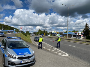 Zdjęcie przedstawiające dwóch policjantów ruchu drogowego. Jeden z nich daje kierowcy znak tarczą drogową do zatrzymania się.