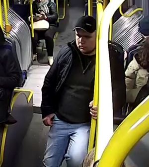 Zdjęcie przedstawiające mężczyznę w autobusie. Mężczyzna trzyma się żółtej poręczy, ma na sobie czarną czapkę z daszkiem, czarną kurtkę, ciemną bluzę i niebieskie, jeansowe spodnie.