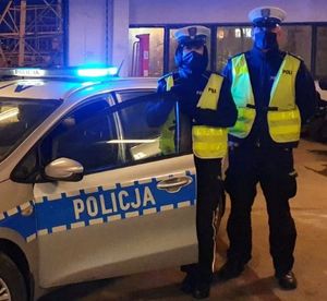 Zdjęcie przedstawiające policjantkę i policjanta z Wydziału Ruchu Drogowego Komendy Miejskiej Policji w Gdyni. Stróże prawa stoją na tle radiowozu.