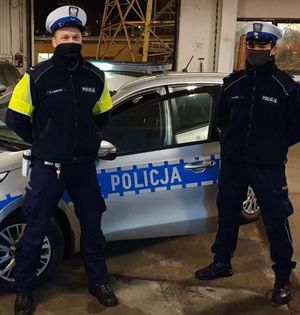 Zdjęcie przedstawiające dwóch funkcjonariuszy z Wydziału Ruchu Drogowego Komendy Miejskiej Policji w Gdyni. Stróże prawa stoją na tle radiowozu.