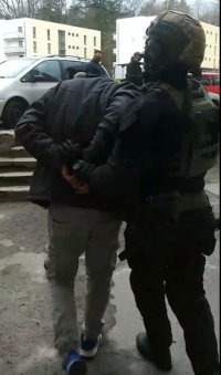 Zdjęcie przedstawiające funkcjonariusza prowadzącego zatrzymanego mężczyznę