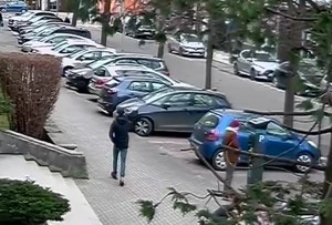 Zdjęcie przedstawiające mężczyznę idącego chodnikiem wzdłuż zaparkowanych samochodów.