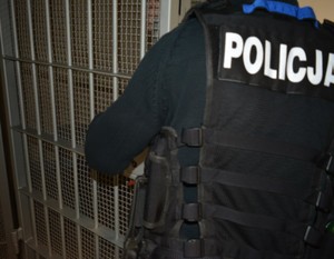 Zdjęcie poglądowe, przedstawiające policjanta zamykającego kratę policyjnej celi.