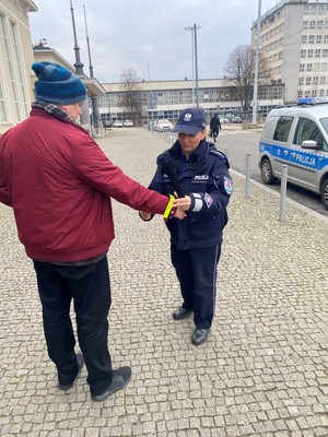 Zdjęcie przedstawiające policjantkę, która przekazuje mężczyźnie opaskę odblaskową