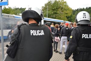 Zdjęcie poglądowe, przedstawiające z tyłu dwóch policjantów w białych kaskach. W tle grupa osób.