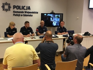 Zdjęcie poglądowe, przedstawiające policjantkę i trzech policjantów, którzy prowadzą konferencję prasową z dziennikarzami. Na fotografii widać dziennikarzy, przygotowujących materiał