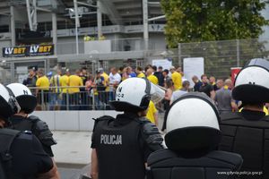 Zdjęcie poglądowe, przedstawiające grupę policjantów na tle kibiców i stadionu.