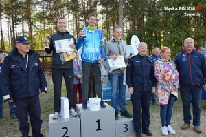 Zdjęcie poglądowe, przedstawiające trzech policjantów na podium. Policjant, który zajął trzecie miejsce, służy w gdyńskim garnizonie. Na zdjęciu jest jeszcze dwóch umundurowanych policjantów oraz kobieta z mężczyzną.