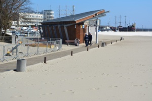 Zdjęcie przedstawiające dwóch policjantów, którzy legitymują mężczyznę na plaży miejskiej.