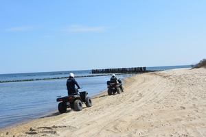 Zdjęcie przedstawiające dwóch policjantów jadących przez plażę na quadach.