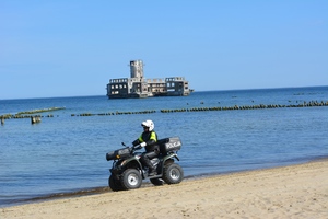 Zdjęcie przedstawiające policjanta jadącego przez plażę na quadzie.