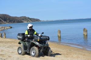 Zdjęcie przedstawiające policjanta jadącego przez plażę na quadzie.