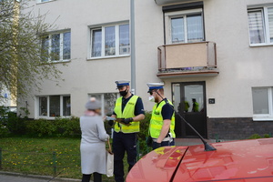 Zdjęcie przedstawiające policjantów którzy przekazują kobiecie maseczkę ochronną.