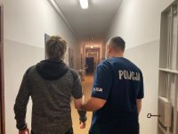 Zdjęcie przedstawiające policjanta, który prowadzi zatrzymanego mężczyznę