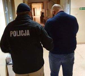 Zdjęcie przedstawiające policjanta prowadzącego zatrzymanego mężczyznę.