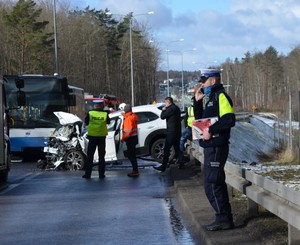 Zdjęcie przedstawiające pracujących policjantów na zdarzeniu drogowym. Z tyłu widać autobus miejski i samochód osobowy.