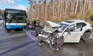 Zdjęcie przedstawiające uszkodzony samochód osobowy oraz autobus miejski. W tle widać strażaków.