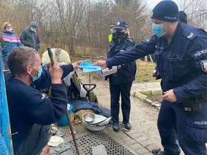 Zdjęcie przedstawiające policjanta, przekazującego osobie bezdomnej maseczkę.