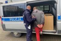 Zdjęcie przedstawiające policjanta, który wprowadza zatrzymanego do radiowozu.