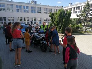 Zdjęcie przedstawiające policjanta i dzieci na tle motocykla