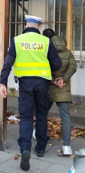 Zdjęcie przedstawiające policjanta prowadzącego zatrzymanego mężczyznę