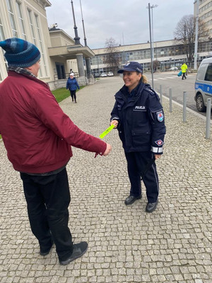 Zdjęcie przedstawiające policjantkę, która przekazuje mężczyźnie opaskę odblaskową