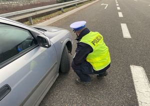 Zdjęcie przedstawiające policjanta ruchu drogowego, sprawdzającego ogumienie opon