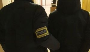 Zdjęcie przedstawiające policjanta prowadzącego zatrzymanego mężczyznę