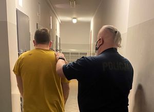 Zdjęcie przedstawiające policjanta prowadzącego zatrzymanego mężczyznę