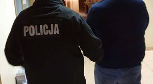 Zdjęcie poglądowe, przedstawiające policjanta prowadzącego zatrzymanego mężczyznę