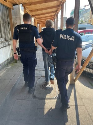 Zdjęcie przedstawiające policjantów prowadzących zatrzymanego mężczyznę