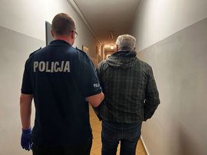 Zdjęcie przedstawiające policjanta prowadzącego zatrzymanego mężczyznę