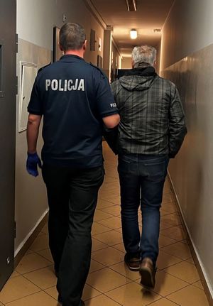 Zdjęcie przedstawiające policjanta prowadzącego zatrzymanego mężczyznę