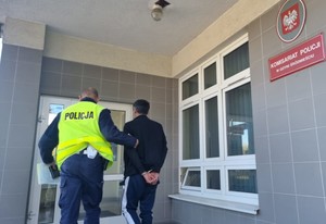 Zdjęcie przedstawiające policjanta prowadzącego do komisariatu zatrzymanego mężczyznę