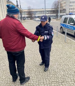 Zdjęcie przedstawiające policjantkę przekazującą mężczyźnie opaskę odblaskową