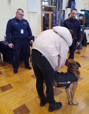 Zdjęcie z targów pracy służb mundurowych, przedstawiające policjantów, studentką i psa służbowego