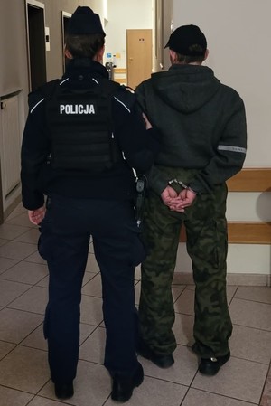 Zdjęcie przedstawiające policjanta prowadzącego zatrzymanego mężczyznę