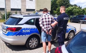 Zdjęcie przedstawiające policjanta prowadzącego zatrzymanego mężczyznę do radiowozu