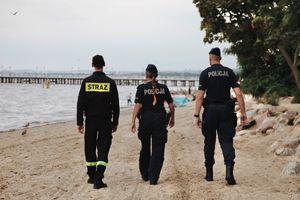 Zdjęcie przedstawiające policjantkę, policjanta i funkcjonariusza Państwowej Straży Pożarnej, którzy patrolują plażę