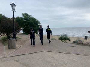 Zdjęcie przedstawiające policjantkę, policjanta i funkcjonariusza Państwowej Straży Pożarnej, którzy patrolują dojście do plaży