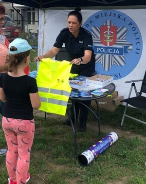 Zdjęcie przedstawiające policjantkę, która przekazuje dziecku kamizelkę odblaskową